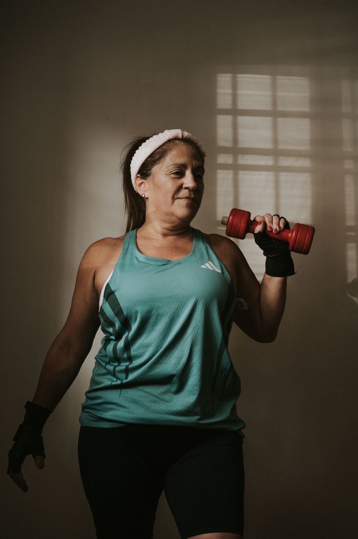 A middle-aged woman in a headband lifting a dumbbell during an indoor workout