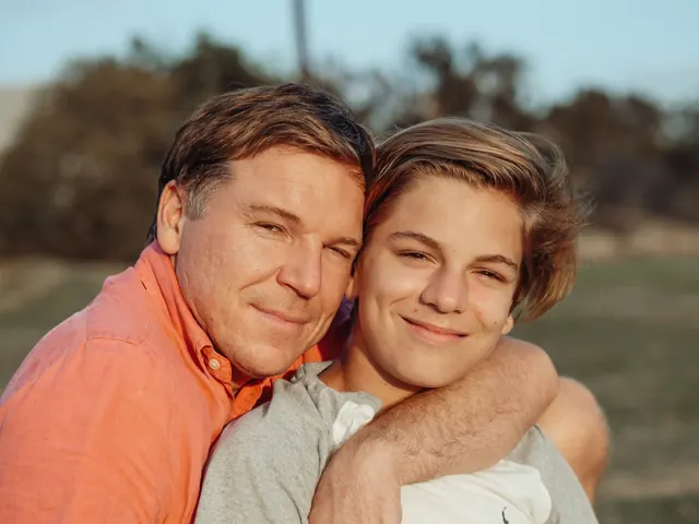 A smiling middle-aged father with his arm around his teenage son outdoors in warm evening light
