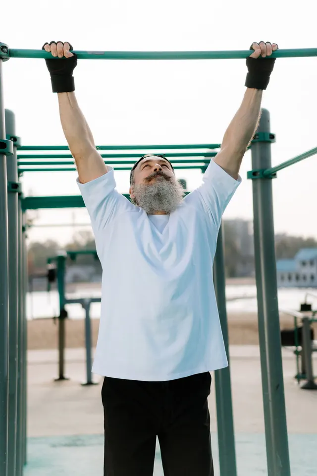 A man with a gray beard doing a pull-up on an outdoor exercise bar